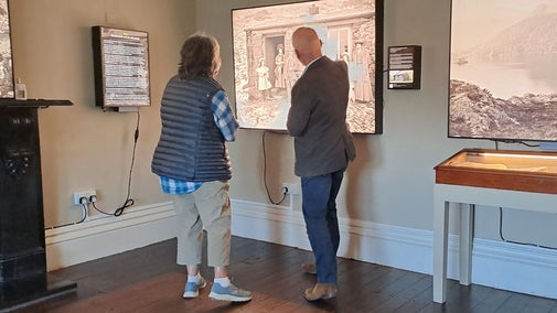 Two people stood in room looking at large lightboxes on wall with black and white landscape photography on